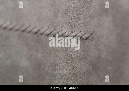 This detailed macro shot showcases a section of refined gray suede leather, accentuated by a robust hand-stitched saddle stitch, highlighting durabili Stock Photo
