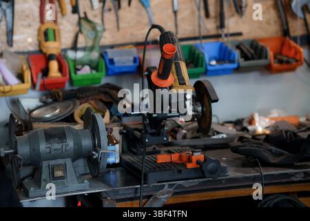 A cluttered workshop scene features two metal grinders on a workbench, surrounded by tools in plastic bins and a leather work glove, depicting a metal Stock Photo