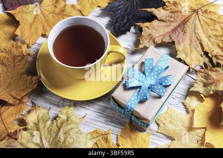 Flat lay autumn composition with gift box and cup of black tea. Time of tea break. Happy thanksgiving congratulation with yellow autumn leaves on vint Stock Photo