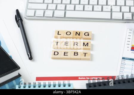 Long term debt concept with letters on cubes. Still life of office workplace with supplies. Flat lay white surface with computer keyboard and financia Stock Photo