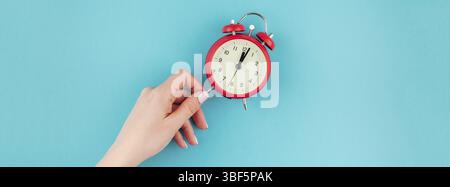 Creative flat lay concept top view of woman hand holding the red vintage alarm clock on bright blue turquoise color paper background with copy space i Stock Photo