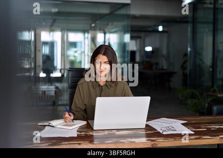 Busy business woman of middle age working on laptop taking notes. Stock Photo