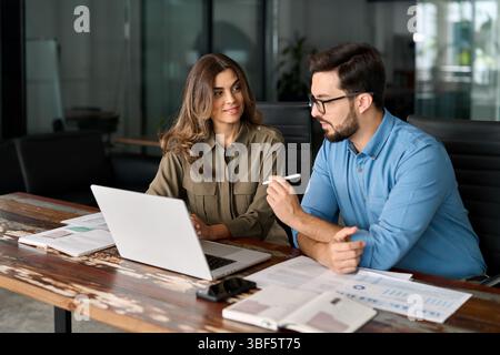 Two busy colleagues working together talking using laptop in office. Stock Photo