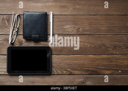 Still life of office workspace with supplies. Flat lay old hardwood desk with black leather wallet and tablet computer. Online shopping and payment. C Stock Photo