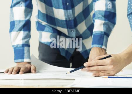 Design project discussing in architecture studio. Architect analyzing paper blueprint. Close up man hand pointing with pencil on construction drawing. Stock Photo