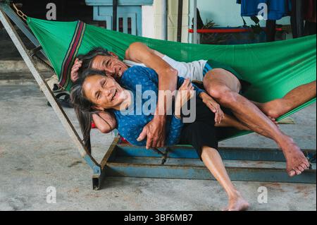 Happy couple of elderly Vietnamese in love hugging on a hammock. Asian old family in the village in Vietnam. Tam Thanh, Quang Nam province, Vietnam - April 10, 2025 Stock Photo