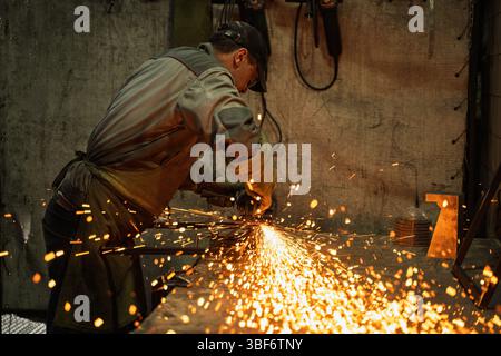Industrial Metalworker Using Angle Grinder in Workshop with Flying Sparks Stock Photo