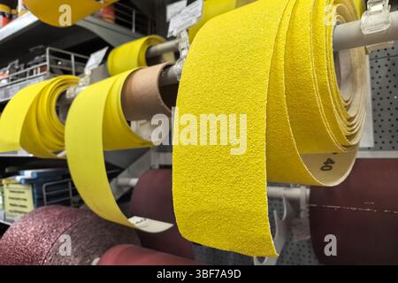 Vibrant yellow sandpaper rolls hang on display in a bustling workshop, drawing attention with their texture. Various grits and colors surround them, i Stock Photo