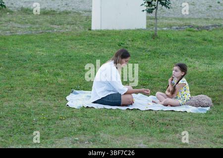 A woman and child relax on a blanket outdoors. The setting is a grassy area with a simple background. They appear calm and content, possibly enjoying Stock Photo
