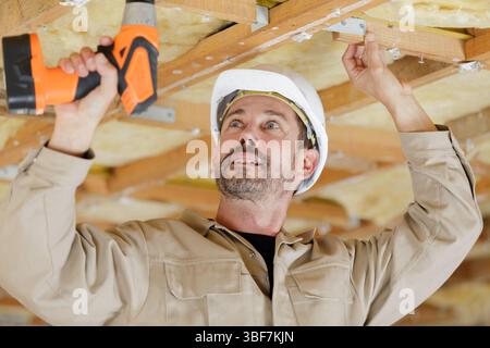 builder using a cordless drill on wooden ceiling joists Stock Photo