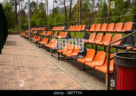 Rows of empty orange plastic seats on the grandstand near the outdoor sports stadium Stock Photo