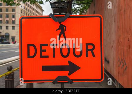 Bright orange pedestrian detour sign with a right-pointing arrow displayed on a city sidewalk. Stock Photo