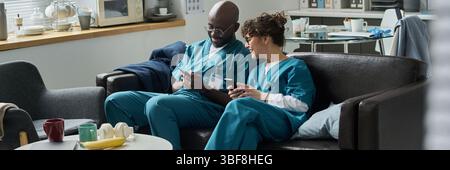 Medical professionals relaxing in hospital lounge during break, sharing information on digital gadgets, connecting and collaborating during downtime Stock Photo