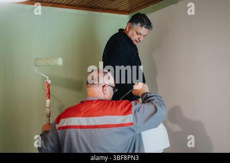 Two Men Collaborating on Painting an Indoor Wall with Light Green Paint Stock Photo