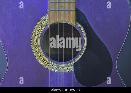 A purple acoustic guitar that hasn't been used for a long time looks dusty, kept standing in a white background frame. Stock Photo