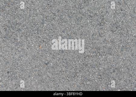 A close-up shot of gray asphalt. Small pebbles and gravel are embedded in the surface, creating a textured and uneven appearance. Stock Photo