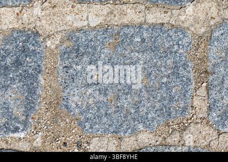 Close-up of irregularly shaped grey stone blocks with beige cement and gravel filling the gaps, forming a rough surface. Stock Photo