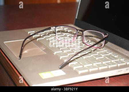A pair of eyeglasses is on the keyboard of a laptop with blurred background. The laptop is resting and it is power off position. Stock Photo