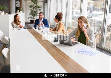 Businesswoman talking over smart phone and professionals discussing strategies and planning project in meeting room Stock Photo