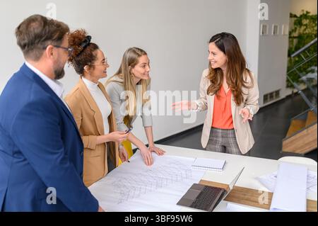Confident female project manager discussing ideas and analyzing blueprint with coworkers in meeting at office Stock Photo