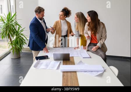 Team of architects reviewing blueprint and planning development strategies while working in office during meeting Stock Photo