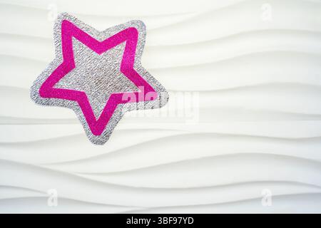 A sparkling star shape features a metallic silver surface with pink outlines, placed on an elegantly textured white background, creating a modern and Stock Photo