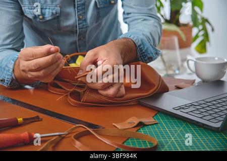 Leather craftsman carefully hand-stitching a stylish bag in his workshop, demonstrating traditional craftsmanship and attention to detail Stock Photo