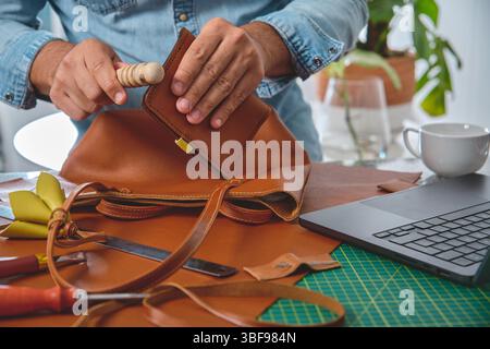 Craftsman burnishing edges of leather bag in his workshop Stock Photo