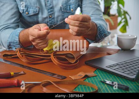 Leather craftsman preparing thread to sew a bag in his workshop, surrounded by tools and technology Stock Photo