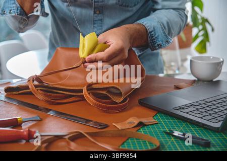 Leather craftsman is sewing a bag handle in his workshop, using traditional techniques and high-quality materials Stock Photo