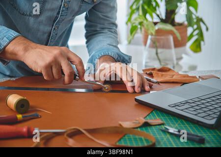 Craftsman using stitching groover and ruler to work leather in his workshop Stock Photo