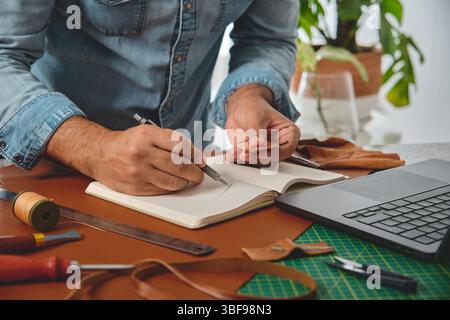 Leather craftsman drawing sketches in notebook for new leather products Stock Photo