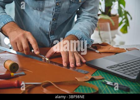 Craftsman using stitching groover and ruler on leather in his workshop, small business and entrepreneurship concept Stock Photo
