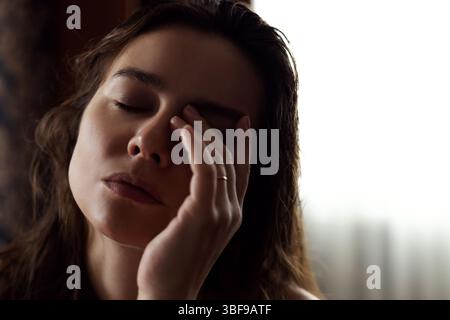 The young woman is tired and very sleepy, holding her hand on her head. Stock Photo