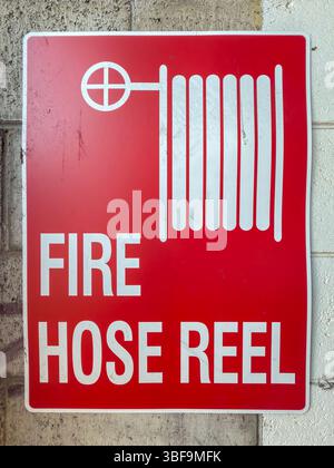 Photograph of an old and dirty red coloured metal Fire Hose Reel sign located on a dirty wall adjacent to firefighting equipment at an industrial site Stock Photo