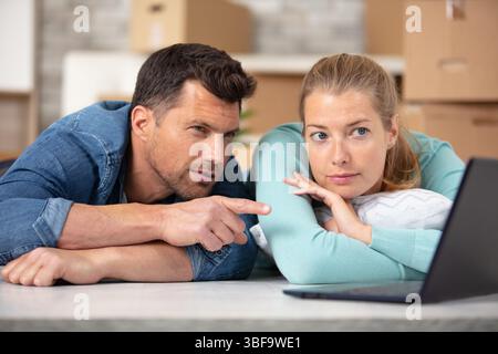 serious couple lay on the floor looking at laptop screen Stock Photo