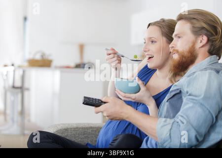 happy young pregnant couple having healthy breakfast while watching tv Stock Photo