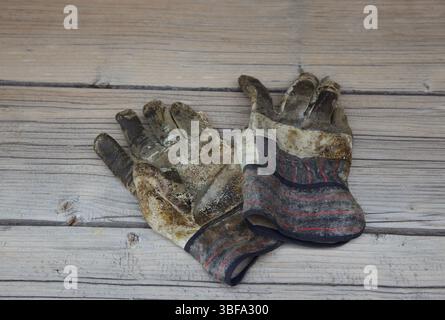 Old, broken and torn work gloves lie on a weathered gray wooden table. Photo Willy Matheisl Stock Photo