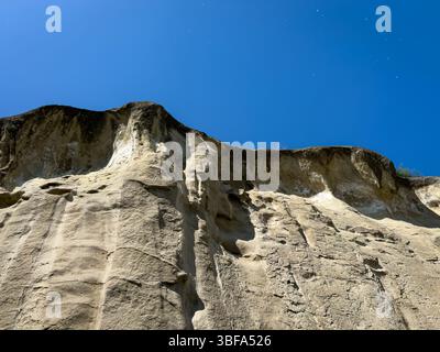 Close-up view of rock cliffs and textured sandstone wall in Uplistsikhe cave city, Georgia, against clear blue sky. No people. Stock Photo