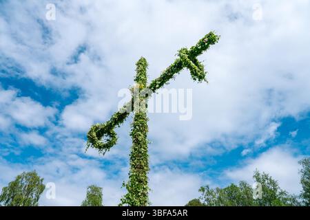 Midsummer celebration in Gammlia, Umea, Sweden, featuring a vibrant maypole adorned with flowers and leaves, set against a backdrop of blue sky and wh Stock Photo