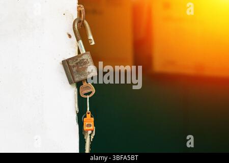 A closeup image of a rusty lock and key hanging on a wall, illuminated by warm sunlight. The scene evokes themes of security, protection, and vulnerab Stock Photo