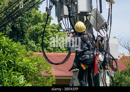 A skilled electrician performs maintenance on overhead power lines, showcasing essential safety practices in an urban environment with lush greenery. Stock Photo
