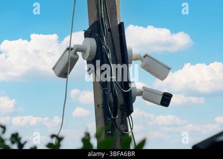 Three security cameras mounted on a telephone pole under a bright blue sky. The image highlights the importance of surveillance technology in urban sa Stock Photo