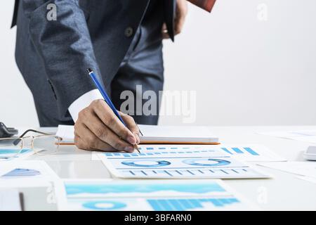 Businessman standing near office desk and analyzing financial charts. Successful corporate manager in business suit and tie. Close-up man hand with pe Stock Photo