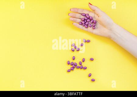 Woman hand holding purple pills handful isolated on bold yellow background with copy space. Template for feminine beauty blog social media. Female hea Stock Photo