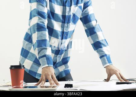 Architect standing near desk with blueprints and cup of coffee. Architecture studio concept with design project. Close up man hand lying on technical Stock Photo