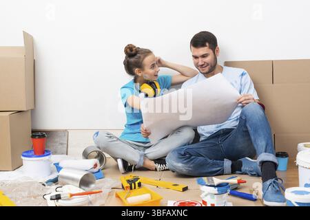 Couple discussing home redesign ideas. Man and woman together planning new home interior design. Cardboard boxes, painting tools and materials on floo Stock Photo