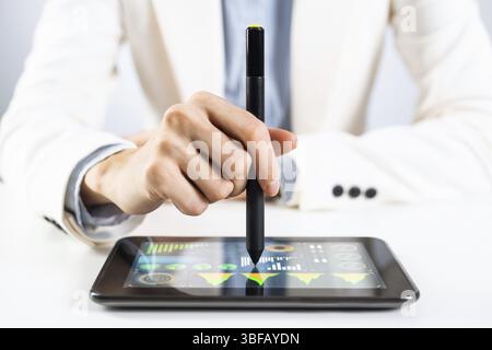 Man in business suit using tablet computer. Close-up of male hands holding pen and tablet gadget. Businessman at workplace in office. Mobile smart dev Stock Photo