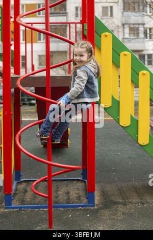 Portrait of beautiful caucasian girl in jeans suit sitting on a playground Stock Photo