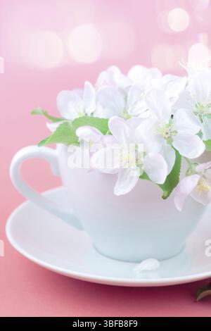 Creative concept of coffee cup and white apple tree blooming flowers on pink background with bokeh and copy space in minimal style, template for text Stock Photo